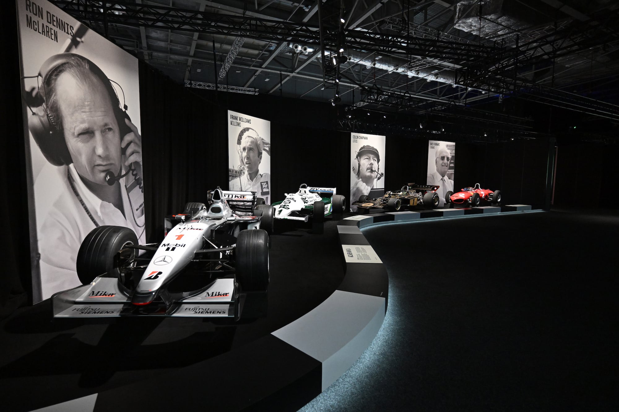 An F1 exhibtion showroom featuring Formula 1 car displays and large-format photos of the teams' engineers and inventors.