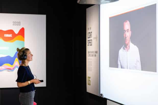 A woman wearing headphones is viewing a screen at the Formula 1 exhibition.