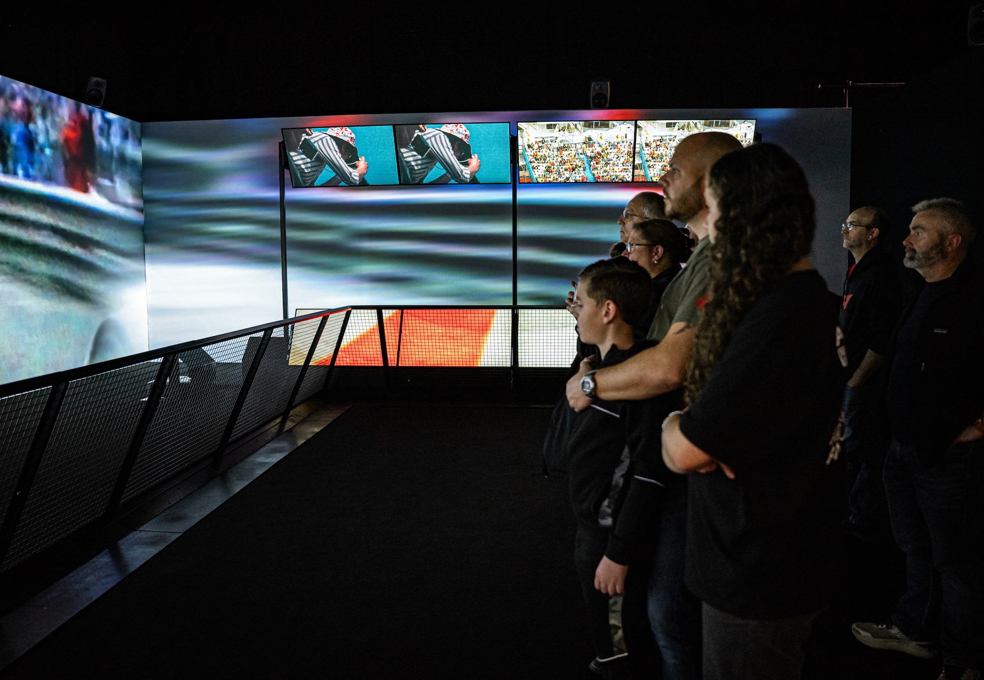 A family group and other visitors watch Formula 1 images on giant screens, immersed in an environment projecting race sequences and driver scenes.